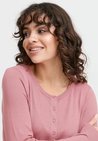 Cardigan rose clair en tissu doux, avec un col rond, des manches longues et six petits boutons sur le devant.