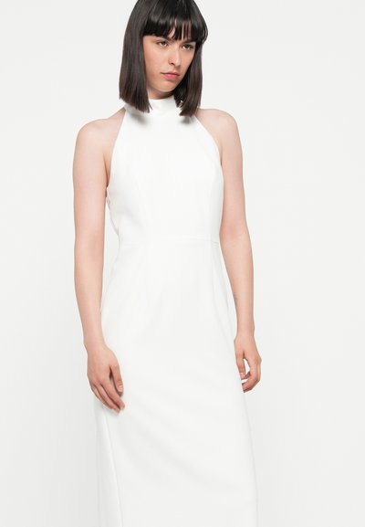 Witte mouwloze jurk met een hoge nek en een getailleerd silhouet. Glad materiaal en minimale stiknaden, die tot aan de enkel reikt.