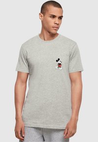 Camiseta de algodón gris con un pequeño estampado en negro y rojo de Mickey Mouse en el área del pecho izquierdo. Corte estándar con mangas cortas.