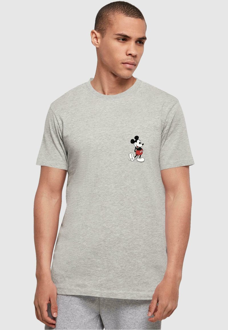 Camiseta de algodón gris con un pequeño estampado en negro y rojo de Mickey Mouse en el área del pecho izquierdo. Corte estándar con mangas cortas.