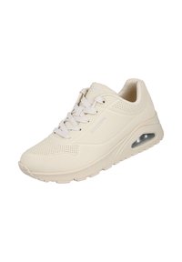 Zapatilla atlética beige con detalles perforados, suela acolchada, cierre con cordones y bolsillo de aire lateral. Presenta una parte superior suave y texturada.