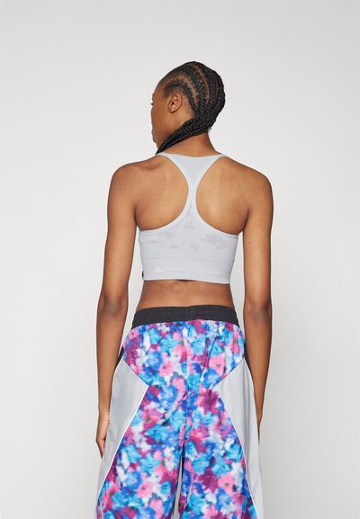 Sivý športový podprsenka s prekríženými ramienkami a textúrovaným dizajnom, spárovaná s farebnými teplákmi s tie-dye vzorom v odtieňoch modrej, ružovej a bielej.