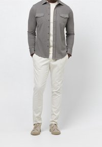 Harmaa pitkähihainen napitettava paita, jossa on rintataskut, yhdistettynä vaaleanbeigeihin housuihin ja vaaleanbeigeihin tennareihin, joissa on yksinkertainen pinta.