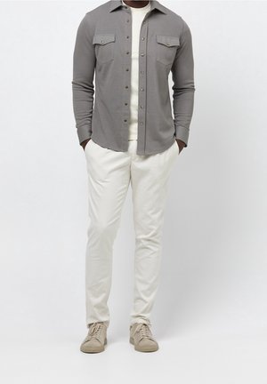 Camisa de botones de manga larga gris con bolsillos en el pecho, combinada con pantalones beiges y zapatillas beiges, con una textura lisa.