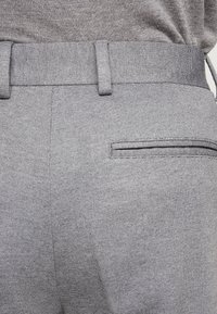 Grå byxor i texturerat tyg, med en rak midjeresår och en bakficka med dragkedja. Minimalistisk design med subtila sömnadsdetaljer.