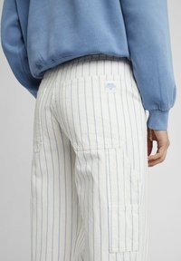 Pantalons cargo blancs rayés avec des rayures bleu clair, dotés d'une poche arrière et d'une étiquette. L'ensemble est associé à un sweat-shirt bleu.