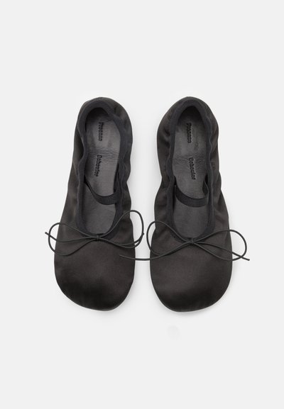 Bailarinas negras de tela suave con punta redonda y un delgado lazo en la parte delantera. Textura suave y diseño minimalista.