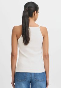 Top de tirantes finos blanco acanalado, con un diseño ajustado. Lleva puesto unos jeans de mezclilla azul, vista desde la espalda. Textura suave.
