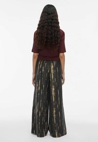 Top court bordeaux associé à un pantalon large noir avec des rayures verticales beiges. Tissu texturé avec une coupe décontractée.