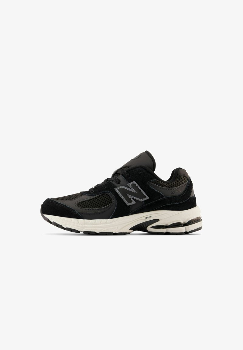 Chaussure de sport New Balance noire et gris foncé avec dessus en mesh et suède, semelle blanche coussinée, et logo "N" sur le côté.