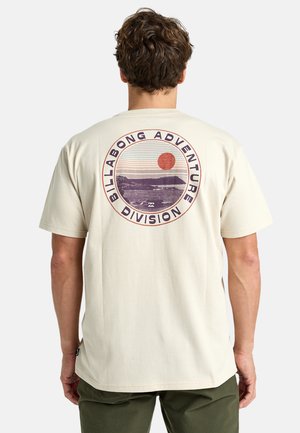 Lichtbeige t-shirt met een ronde opdruk die een zon en bergen omvat. Korte mouwen en een comfortabele pasvorm, gemaakt van zachte stof.