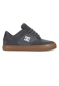 Chaussure de skate basse gris foncé avec col rembourré, lacets gris, logo DC blanc sur le côté et semelle en caoutchouc naturel.