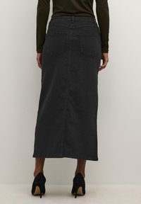 Jupe maxi en denim noir avec une coupe droite, poches arrière et une taille ajustée, associée à des chaussures à talons hauts noires.