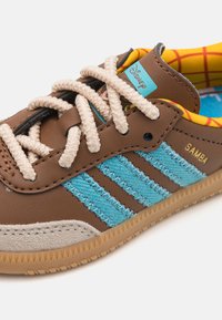 Brown leather shoe with blue stripes, beige toe cap, and textured sole. Features light cream laces and colorful inner lining with Disney design.