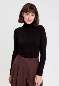 Sort ribbet langærmet turtleneck sweater kombineret med højtaljede brune plisseebukser. Blød stoftekstur, tætsiddende design.