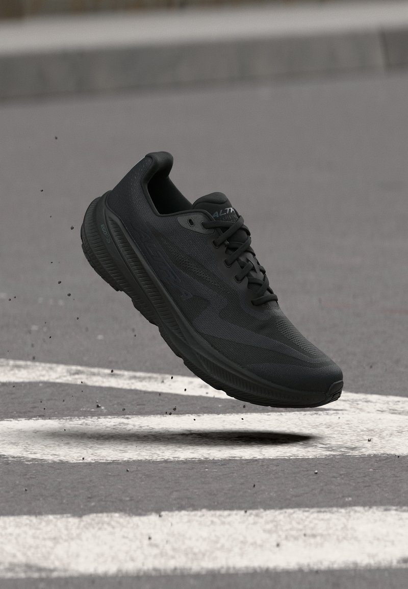 Μαύρο αθλητικό παπούτσι για τρέξιμο αιωρείται πάνω από γκρι άσφαλτο με λευκές γραμμές δρόμου και μικρά συντρίμμια.