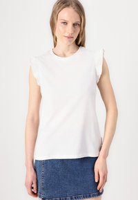 Tricou alb din bumbac cu mâneci umflate. Are o croială lejeră și un gât rotund. Asortat cu o fustă din denim.