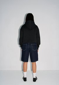 Czarna krótka bluza z kapturem, zestawiona z ciemnoniebieskimi dżinsowymi szortami. Białe skarpetki do kostek i czarne buty dopełniają całość.