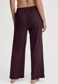 Donkerpaarse wijde broek met een elastische tailleband, gemaakt van een zachte, rekbare stof. De pijpen zijn losvallend en reiken tot de enkels.