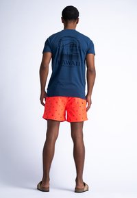 Tricou navy cu un grafic de val și textul "HAWAII Waveriders" pe spate, asortat cu șorturi de baie portocalii strălucitoare, cu mici modele navy.