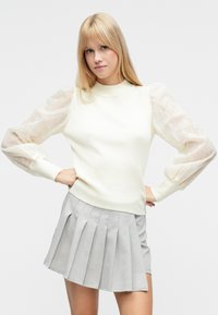 Norsunluunvärinen villapaita, jossa on resorikuvio ja pulleat, läpikuultavat hihat, yhdistettynä vaaleanharmaaseen laskostettuun hameeseen. Rentoa, yksinkertaista muotoilua pehmeillä väreillä.