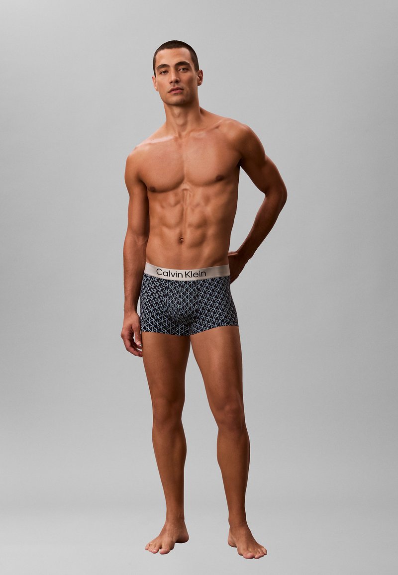 Boxers ajustados de color negro con patrón geométrico y una suave cinturilla elástica que presenta el logo de Calvin Klein. Textura de tela suave, diseño ceñido.