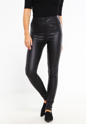 Pantaloni skinny neri in similpelle con un alto cintura, texture morbida e design aderente, abbinati a stivali neri alla caviglia.