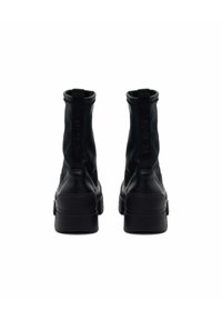 Bottines noires avec une finition en cuir lisse, des côtés élastiques et une semelle en caoutchouc épaisse. Détails du logo à l'arrière.