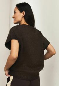 Brun kortærmet striktrøje med ribbet kant og afslappet pasform. Tekstureret stof viser subtile variationer, med en bred rund halsudskæring.