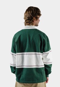 Grønn- og hvitstripet genser med krage, med bordauxfargede aksentlinjer, laget av teksturert bomullsmateriale. Synlige sømdetaljer.