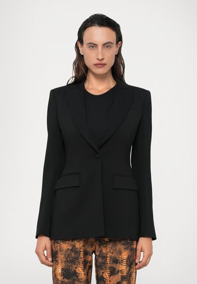 Sacou negru personalizat cu un singur nasture, rever înclinat și două buzunare frontale, asortat cu pantaloni cu model portocaliu și negru.