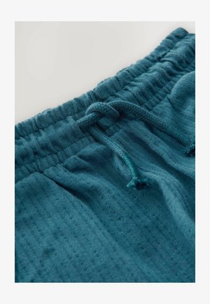 Teal värvi puuvillased lõõgastuspüksid tekstuurse mustriga, elastne vöökoht ja eespaeladega kinnitus.