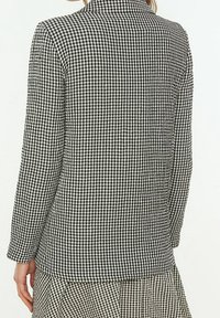 Sorte og hvide gingham-mønstrede skjorte med lange ærmer og krave, der har en slim fit og struktureret design. Bagfra ses en knapfri afslutning.