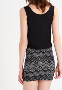 Haut sans manches noir associé à une mini jupe à motifs présentant des designs géométriques en noir et blanc, en tissu texturé et de forme ajustée.