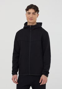 Felpa nera con zip e cappuccio, caratterizzata da una texture liscia e un audace design delle cuciture sul petto. Vestibilità slim con maniche lunghe.