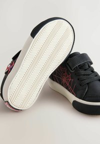 Zwarte sneakers met een rood spinnenwebontwerp, met een glad bovenwerk, een gestructureerde band en een rubberen zool met een zigzagprofiel.