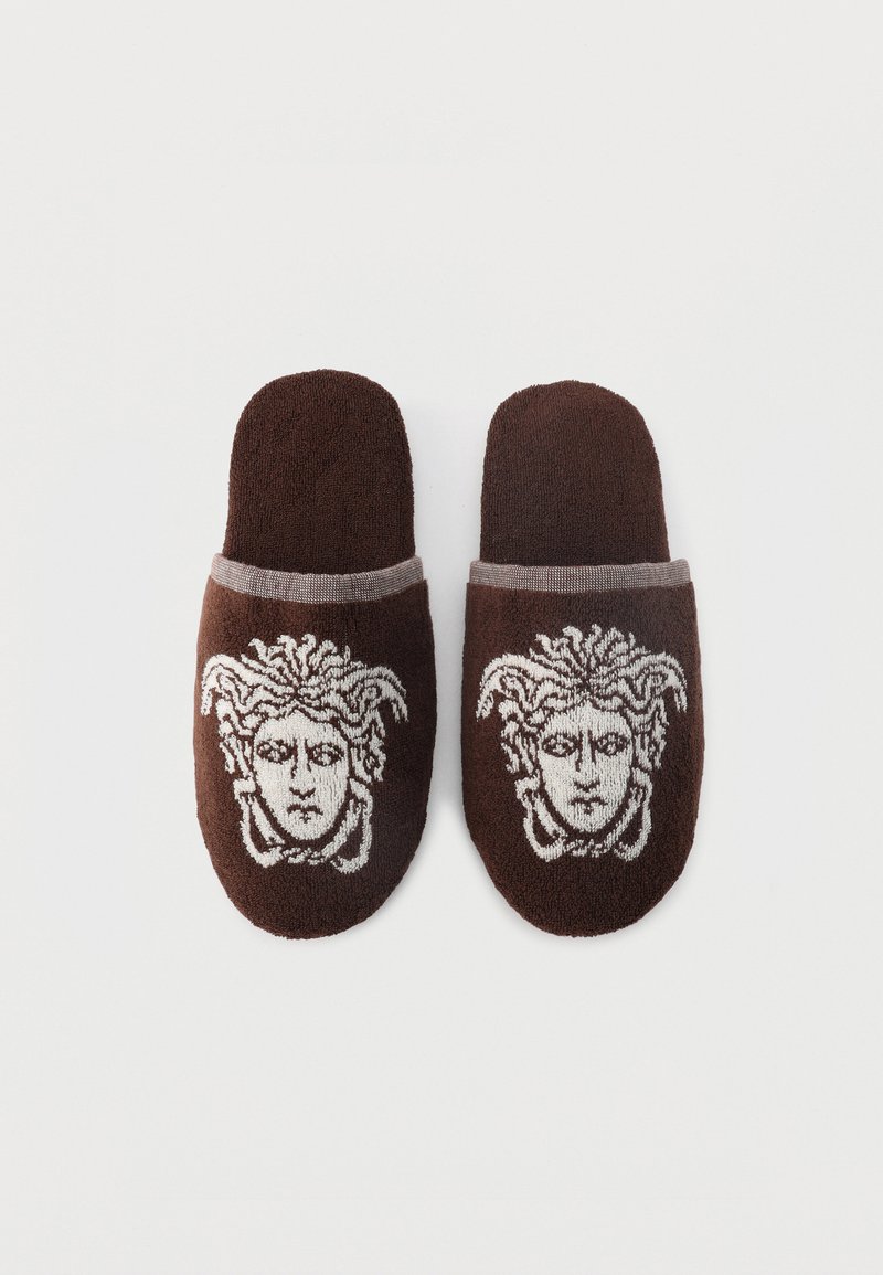 Coppia di pantofole marroni con ricamo della testa di Medusa in bianco su ogni parte superiore, con tessuto testurizzato e punte chiuse arrotondate.