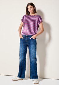 Lilla og hvid stribet kortærmet top parret med blå vide jeans. Jeansene har en let falmet tekstur og fem lommer.