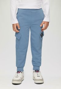 Hellblaue Sweatpants mit elastischem Bund, zwei seitlichen Taschen und zwei aufgesetzten Cargo-Taschen. Kombiniert mit weißen Sneakers, die graue Akzente aufweisen.