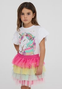T-shirt bianco con maniche arricciate che presenta una grafica di un unicorno. La gonna ha tulle con strati di tonalità rosa, giallo e verde. Texture morbida.