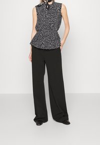 Top peplum floreale nero con dettaglio al collo legato, abbinato a pantaloni neri dal fit morbido e scarpe nere a punta. Tessuto liscio e vestibilità rilassata.