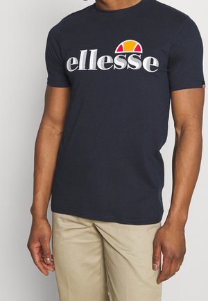 Mørkeblå bomulds t-shirt med korte ærmer, der har et stort hvidt "ellesse" logo og en farverig halvcirkelformet accent over teksten.