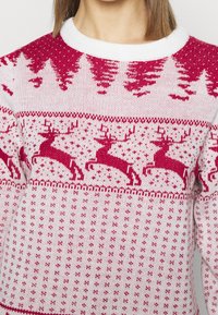 Röd och vit stickad tröja med en festlig design med renar och tallar, rund hals och strukturerade mönster.