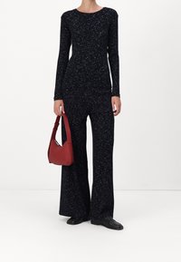 Zwarte jumpsuit met lange mouwen en een gestippeld patroon; gecombineerd met een rode schoudertas en zwarte schoenen, met een getailleerde silhouet en uitlopende pijpen.