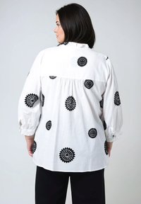 Witte blouse met zwarte bloemige borduursels, losse pasvorm, geplooide achterkant, knoopmanchetten en een zacht gestructureerde kraag.