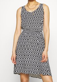 Robe noire et blanche à motif, au design sans manches, avec une taille élastique et un ourlet fluide, présentant une texture à imprimé géométrique.