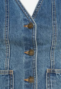 Δερμάτινο γιλέκο με πέντε χάλκινους κουμπιά, δύο μπροστινές τσέπες και πορτοκαλί ραφή. Η υφή είναι λεία με κλασικό μπλε χρώμα.