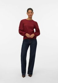 Burgundy texturerad långärmad topp med rund halsringning och rynkade ärmar, kombinerad med mörkblå vida jeans och bruna spetsiga klackar.