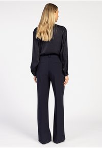 Zwarte blouse met lange mouwen en een licht doorzichtige textuur, gecombineerd met aansluitende, marineblauwe high-waisted broek met een getailleerde silhouet.