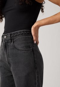Jeans noirs taille haute avec un détail de ceinture tressée et un design à cinq poches, affichant une texture lisse et une coupe slim.